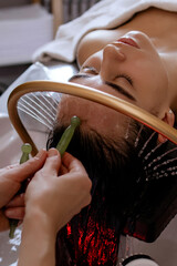 Close-up of a woman receiving a relaxing Japanese head spa treatment, with green massage sticks applied to her scalp, while water gently flows from a special tool during the session in a beauty salon