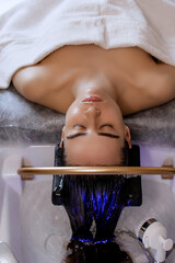 Close-up of a woman receiving a head massage during a Japanese head spa treatment with water flowing from a special hair washing tool, focusing on the scalp relaxation and beauty therapy