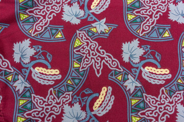 A close-up shot of a fabric with a traditional batik pattern, featuring a deep red background adorned with intricate floral and geometric motifs.