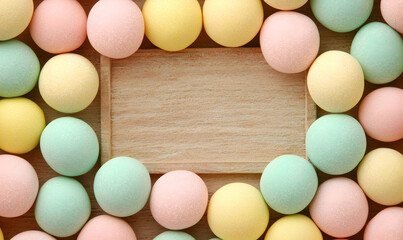 Colorful candy arranged around a light wooden rectangle, pastel, yellow, pink, green, round