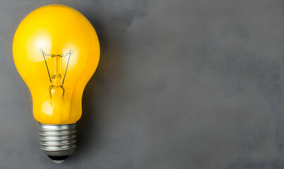 Yellow lightbulb on gray background. Tungsten filament visible. Conceptual image of innovation and inspiration