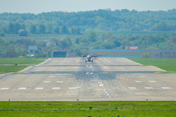 Military aircraft approaches runway during a clear day in a rural airfield surrounded by lush...