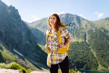 Naklejka premium Woman hiker with bright hiking backpack on top of mountain overlooking mountain landscape. Young woman enjoying view and feeling freedom outdoors. Hiking concept.