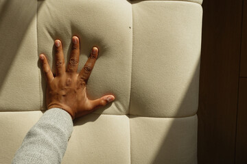 Person pressing hand on soft fabri csofa surface in a bright room