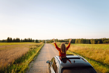 Cute woman enjoying road trip leaning out of car window. Beautiful female traveler in car at...