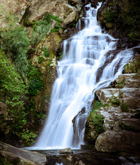 Obraz premium A breathtaking view of a cascading waterfall nestled in a lush, green forest. The water flows gracefully over rugged rocks and boulders, creating a serene and tranquil atmosphere.