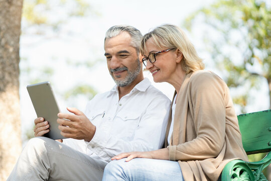 Technology connect and modern elderly lifestyles concept. Aged senior couple waving hands greeting grandkids via facetime video call internet conference outdoors in the park
