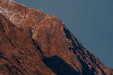 mountain summit and ridge. dramatic steep red stone cliff in sun light with light snow cover,...