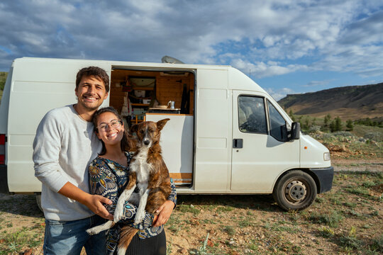 Happy couple with dog hugging in front of camper van