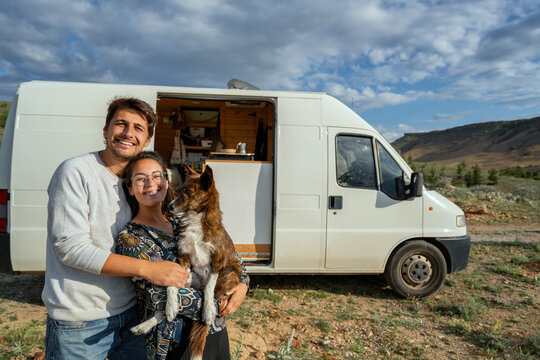 Happy couple with dog hugging in front of camper van