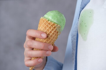 Close up melting mint ice cream in waffle cone in the background dirty stain on white clothes. indoors, likely enjoying a warm day and a sweet treat.
