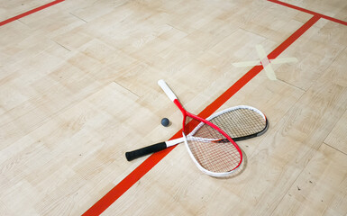 Two rackets and two squash balls lie on the parquet floor. Horizontal photo