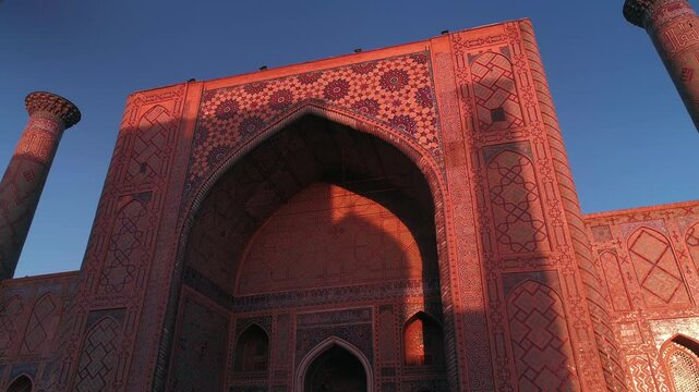 A drone flies near a complex Bibi-Khanym Mosque in Samarkand, Uzbekistan. The building is illuminated by the pink dawn light. Cloudless morning.
