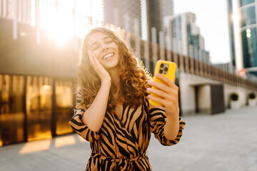 Beautiful tourist with phone walks with view of metropolis. Young woman blogs with phone at sunset....