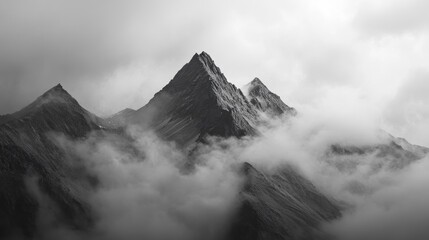 Dramatic black and white photo of three majestic mountain peaks shrouded in mist and clouds.