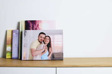 Canvas with different printed photos on wooden chest of drawers near white wall, space for text