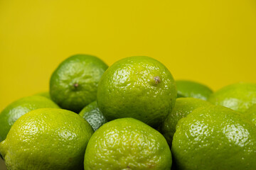 Whole fresh limes fruit on yellow background close-up.