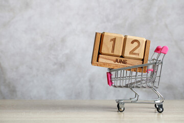 Shopping cart carrying wooden calendar showing june 12th representing upcoming sales