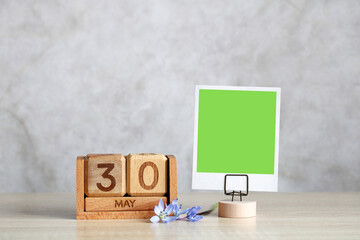 Wooden perpetual calendar showing may 30th with green screen photo frame and flowers