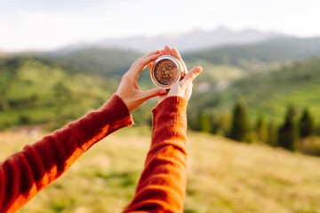 A beautiful woman in a hat and holding a compass stands on a green hill with a stunning view. Young...