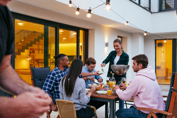 A group of young diverse people having dinner on the terrace of a modern house in the evening. Fun for friends and family. Celebration of holidays, weddings with barbecue