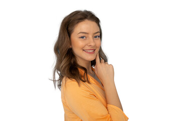 Young woman with long brown hair, wearing orange shirt, touching chin and gently smiling, studio...