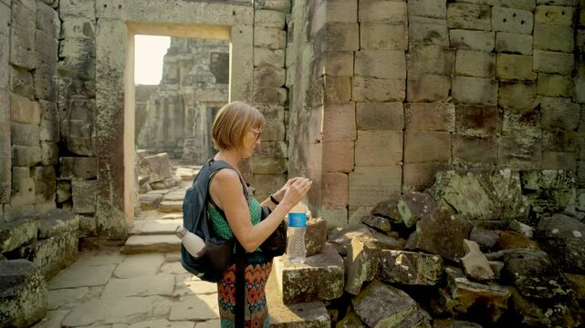 Backpacking traveler photographing Khmer stone carvings in Preah Kohn Angkor Wat