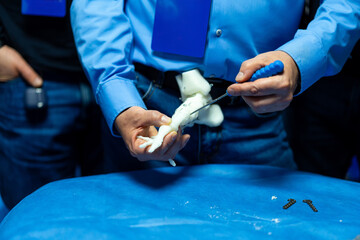 Surgical technique demo on model. A person shows a surgical technique on a model at a blue table as others watch in a workshop.