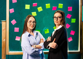 Women in creative collaboration. Two women confidently pose in a colorful workspace filled with...