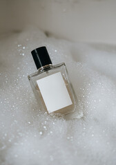 Clear glass perfume bottle with blank label, nestled in a bath of suds