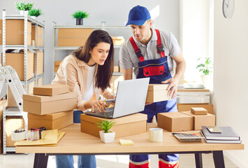 Man and woman working together in a parcel warehouse, conducting inventory using a laptop. Teamwork...
