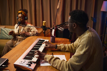 African American dj playing synthesizer while woman singing song during online podcast in studio