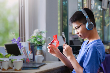 Asian schoolboy sitting near window and doing homework at home by learning various leaves and flowers by using magnifying glass and laptop, now he is learning about indian shot leaf and canna flower.