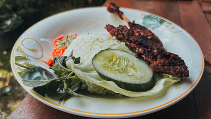 Traditional Indonesian grilled duck (bebek bakar) served with steamed rice, fresh cucumber slices, raw cabbage, and mixed vegetables. 