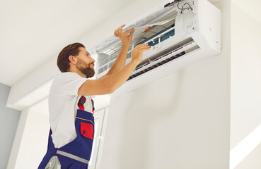 Workman from air conditioning installation and warranty maintenance service setting up modern indoor AC unit on room wall inside new flat or office, repairing something, or removing old purifier parts