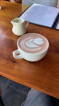Coffee cup with leaf drawing in a restaurant or cafe shop. POV from phone or food critic content creator influencer filming table. UGC vlog style. Tasty drink in hip place. User generated content