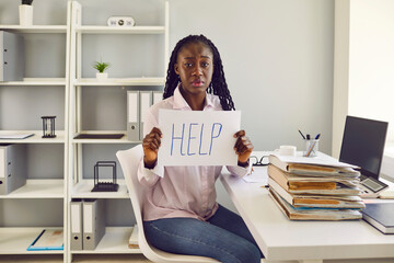 African american upset overworked woman sitting at the desk at her workplace in the office with a...