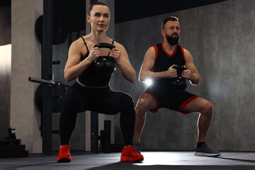 Fototapeta premium Athletic couple training with kettlebells in gym
