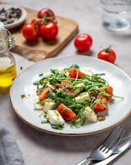 Healthy arugula salad with cherry tomatoes, mozzarella and pesto sauce on a light background