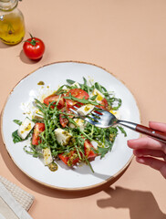 Hand holding fork fresh arugula salad with cherry tomatoes, mozzarella, pesto sauce
