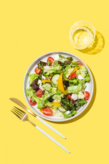Vegetable salad with lettuce, olives and feta cheese on yellow background