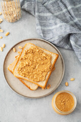 Peanut butter toast on a plate on a light background with nuts, napkin and morning shadow.