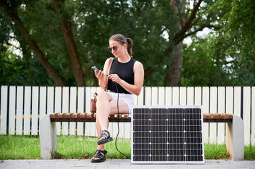 Woman connecting smartphone to photovoltaic solar panel. Integration of sustainable renewable...
