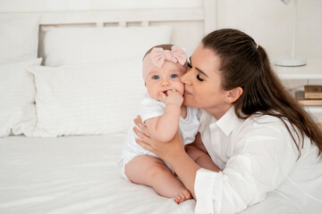 mom and baby hug and kiss at home on the bed in the bedroom, parental love and care, happy motherhood, mom with a baby in her arms, space for text