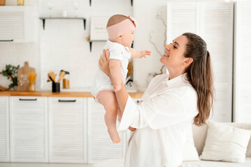 Fototapeta premium mom and baby hug and kiss at home in the bedroom, parental love and care, happy motherhood, mom with a baby in her arms, space for text