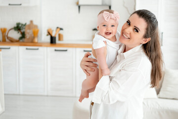 Obraz premium mom and baby hug and kiss at home in the bedroom, parental love and care, happy motherhood, mom with a baby in her arms, space for text