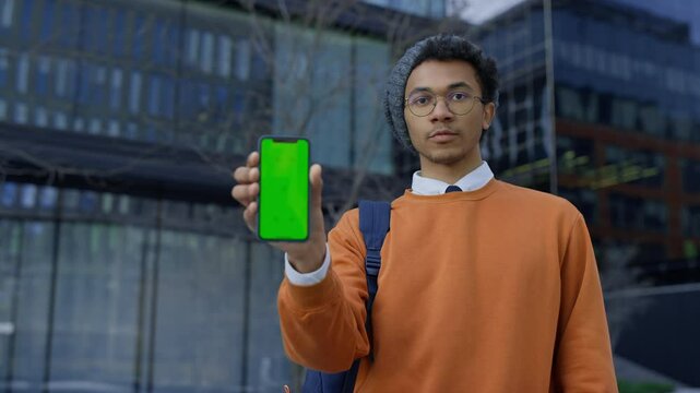 Student showing smartphone with green screen outside