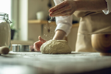 A baker in an apron kneads the dough with his hands and sprinkles it with flour to bake delicious homemade bread.