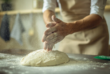 A baker in an apron kneads the dough with his hands and sprinkles it with flour to bake delicious homemade bread.