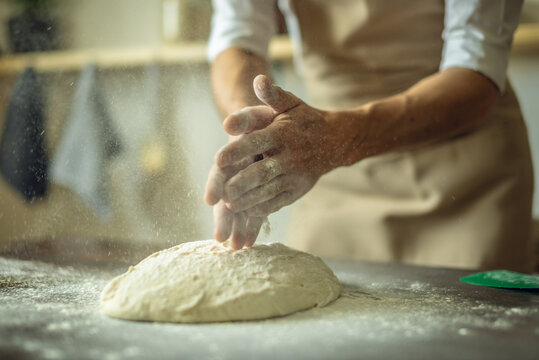 A baker in an apron kneads the dough with his hands and sprinkles it with flour to bake delicious homemade bread.